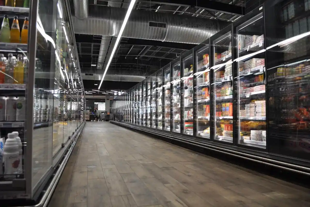 commercial-walk-in-cooler-installation-south-ogden-utah Grocery store aisle in Ogden, Utah showcasing energy-efficient commercial refrigeration systems with glass door display freezers and overhead HVACR ducting.