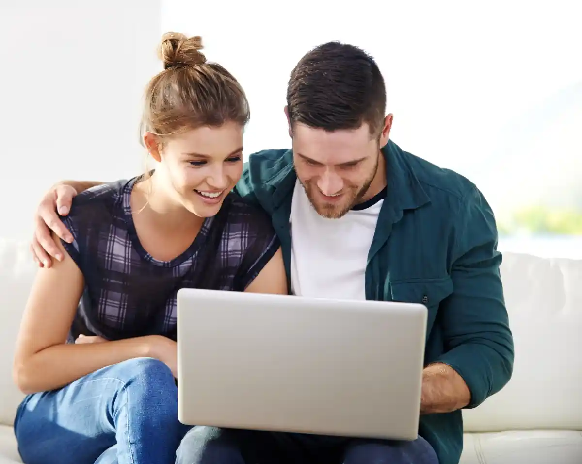 A smiling couple reviews flexible plumbing financing options on a laptop at home after scheduling service with Utah Mechanical Systems in Ogden, Utah.